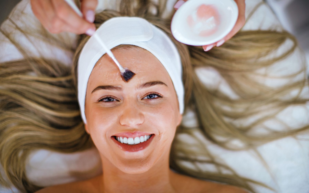 Mujer sonriente durante un tratamiento facial profesional de peeling químico en clínica médica estética, realizado con brocha por especialista en Madrid.
