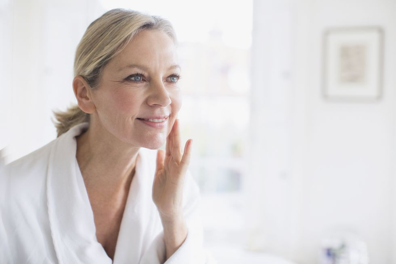 sueroterapia-revista-diez-minutos-belleza-doctora-trasmonte Mujer madura con piel luminosa mirándose al espejo tras recibir sueroterapia, ilustrando los beneficios explicados por la Dra. Victoria Trasmonte en la revista Diez Minutos.