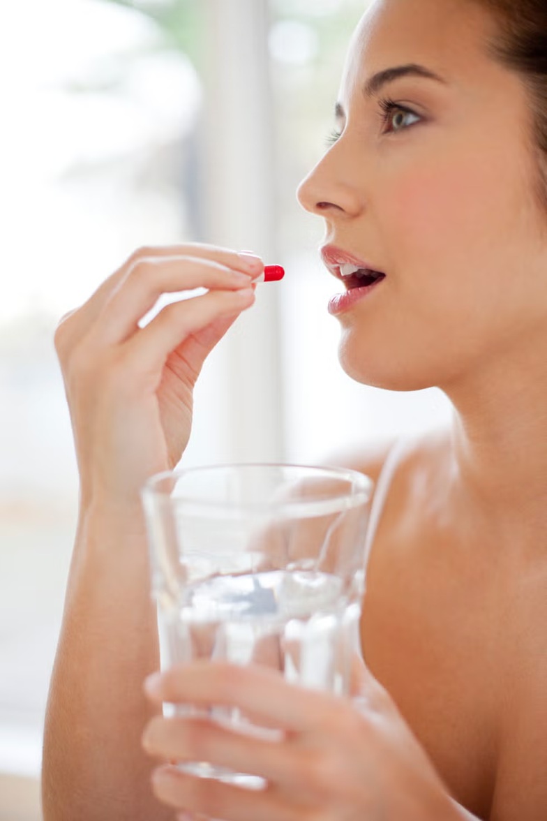 Mujer tomando suplemento con agua, imagen relacionada con magnesio y vitamina B6 para mejorar el sueño, reducir la retención de líquidos y la inflamación facial