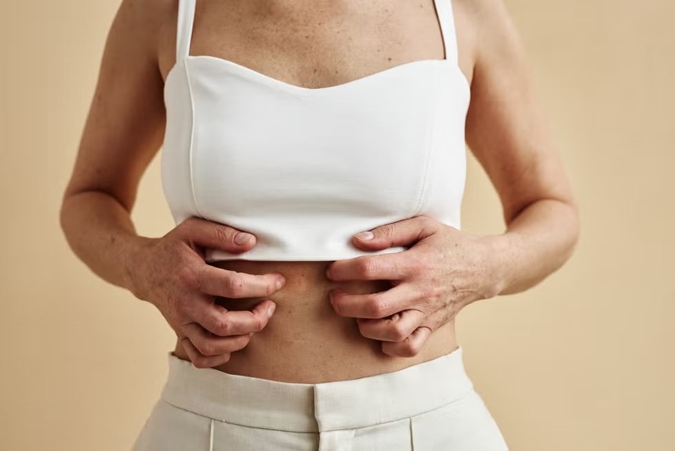 Mujer pellizcando suavemente la piel del abdomen con ambas manos para señalar la zona donde se puede localizar grasa abdominal